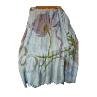 Un foulard Innbamboo O’Keeffe bleu clair, orné d’un grand motif floral abstrait dans des tons de violet et de vert, avec un ourlet effiloché.