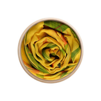 Un foulard en bambou Innbamboo De Chirico – disponible en deux coloris, orné d'un motif jaune et vert – est soigneusement enroulé dans une boîte ronde en bois, de sorte qu'il ressemble à une rose lorsqu'on le regarde d'en haut.