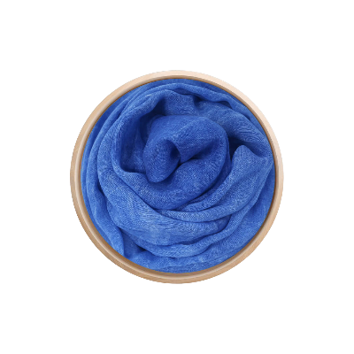 Un foulard en bambou Innbamboo Tinta Unita de couleur bleu pâle, soigneusement enroulé dans une boîte circulaire en bois clair, vu de dessus sur un fond blanc.