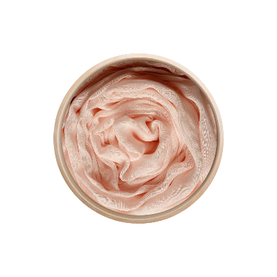 Un récipient rond contient le foulard en bambou Innbamboo Tinta Unita – 3 coloris, dont le tissu rose pâle et soyeux est soigneusement disposé à l'intérieur en formant un motif ondulé délicat, semblable à une rose.
