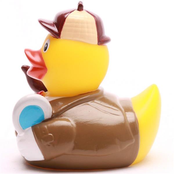 Canard en caoutchouc jaune déguisé en détective, vêtu d'un manteau et d'un chapeau marron, tenant une loupe bleue et une pipe marron, tourné vers la gauche.
