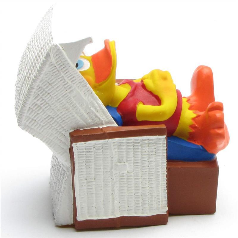 Une figurine de canard de bande dessinée jaune est allongée dans un lit, en train de lire un grand livre ouvert qu'elle tient au-dessus de sa tête. Le canard porte une chemise rouge et des chaussures orange ; il a l'air détendu et concentré sur son livre.