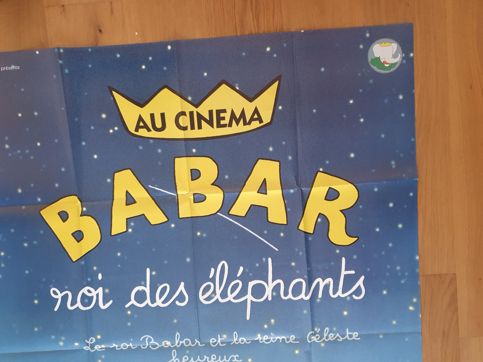 Voici une description remaniée à partir des données fournies sur le produit : L'« Affiche de cinéma Babar, roi des éléphants – 120 × 162 cm » présente un fond bleu parsemé d'étoiles, sur lequel figure une couronne portant l'inscription « Au Cinéma » au-dessus du mot « Babar » écrit en lettres jaunes bien visibles. La mention « roi des éléphants » apparaît en blanc en dessous, et une petite illustration représentant un éléphant est située dans le coin supérieur droit.