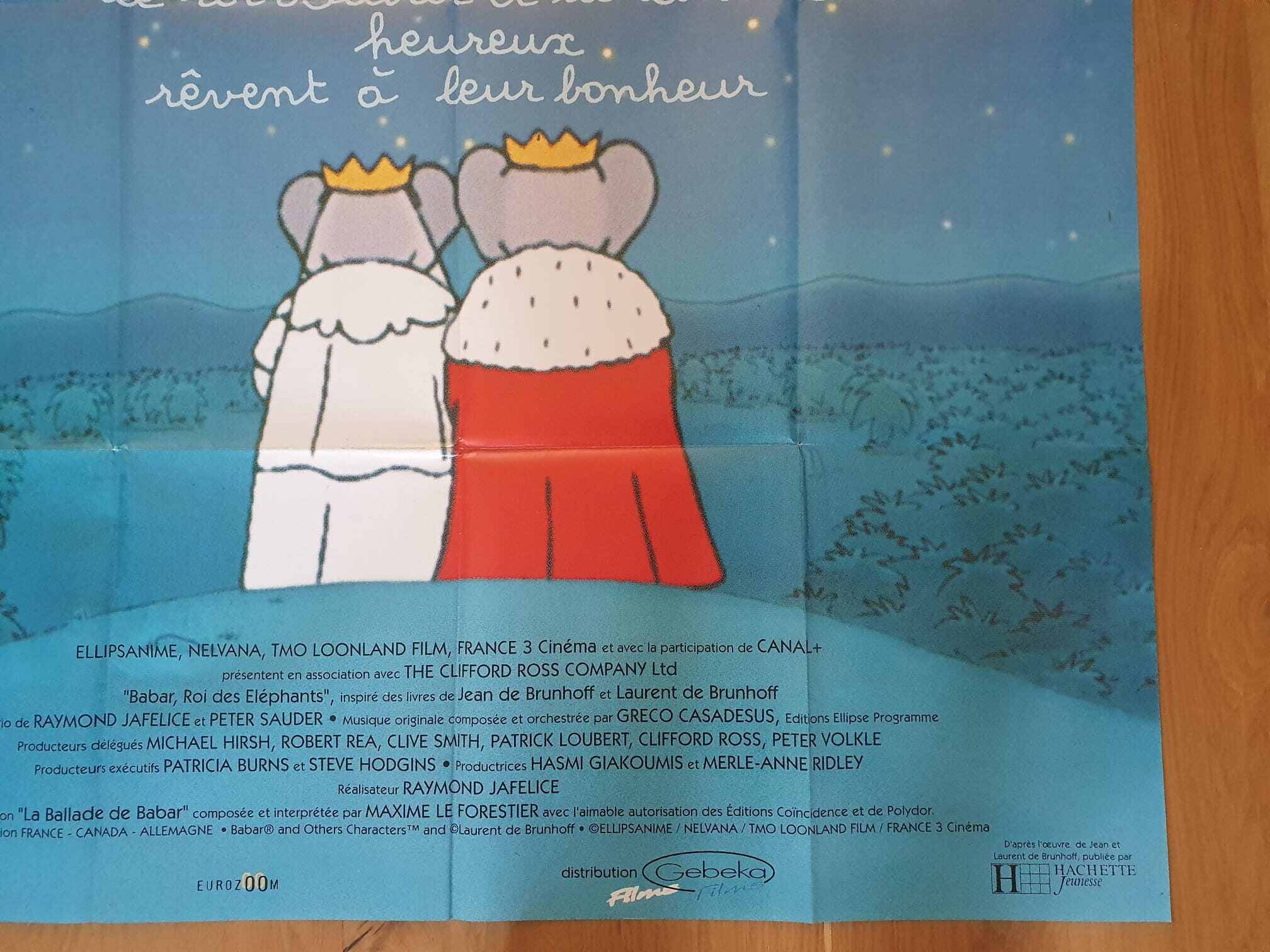 Affiche de cinéma « Babar, roi des éléphants » – 120 × 162 cm : Deux éléphants coiffés de couronnes et parés de capes royales se tiennent côte à côte, dos tournés. Sur fond bleu, un texte en français figure en haut de l’affiche et les crédits de production apparaissent en bas, évoquant une ambiance royale ou celle d’un conte pour enfants.