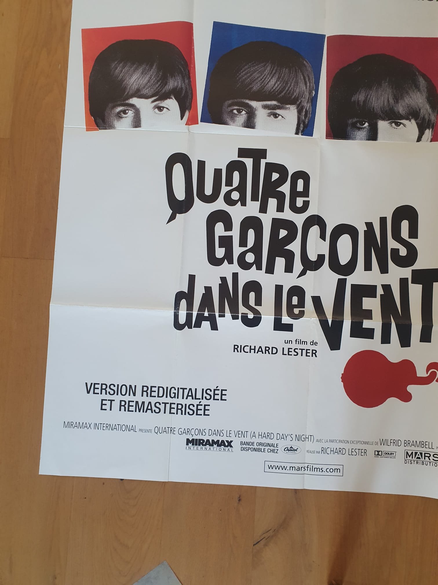 Affiche de cinéma « The Beatles – Quatre garçons dans le vent » (120 × 161 cm), comportant en haut des photos en noir et blanc partiel représentant les visages de quatre jeunes hommes, ainsi qu’un texte stylisé en gras accompagné d’une silhouette de guitare rouge sur fond blanc.