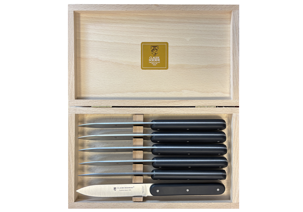 Un coffret de 6 couteaux de table Claude Dozorme Navette 6.16 – Manche noir mat, comprenant six couteaux à steak au manche noir mat, soigneusement rangés dans un coffret en bois dont le couvercle est ouvert pour laisser apparaître une étiquette Claude Dozorme dorée à l'intérieur.