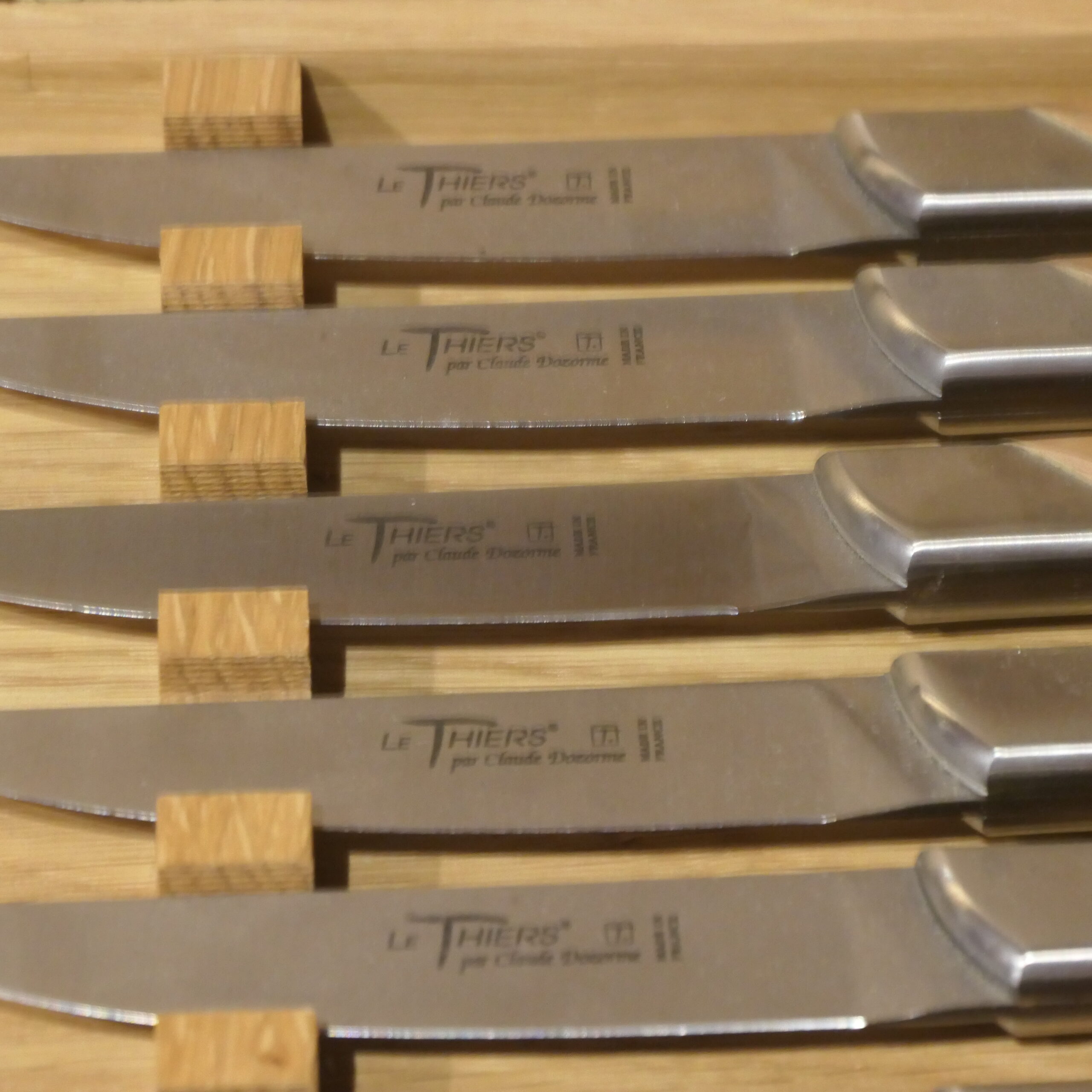 Six couteaux en acier inoxydable avec des manches en bois sont soigneusement rangés dans un porte-couteaux en bois ; chaque lame porte la gravure « Le Thiers par Claude Dozorme ».