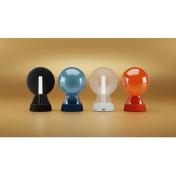 Quatre lampes « Mr Bio » de la marque Xoopar, dotées chacune d'un abat-jour rond en verre et d'un socle coloré — noir, bleu, blanc et orange —, sont alignées côte à côte sur un fond beige.