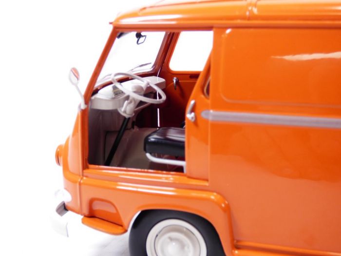 Gros plan sur la miniature Norev « Voiture » représentant une Renault Estafette de 1959 de couleur orange (échelle 1/18), dont la portière conducteur est ouverte, dévoilant le volant et le siège noir, sur fond blanc.