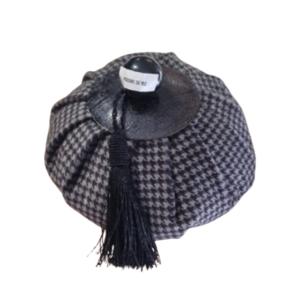 Un récipient rond, recouvert de tissu à motif pied-de-poule noir et blanc, surmonté d'un pompon noir et d'un petit bouchon portant l'inscription « POUDRE DE RIZ » sur fond blanc.
