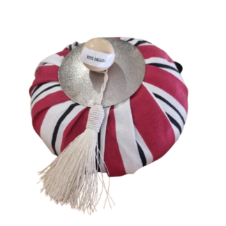 Un objet rond, recouvert de tissu à rayures rouges, blanches et noires, surmonté d’un disque argenté, d’un pompon blanc et d’un petit dôme portant l’inscription « ROSE PASSION ».