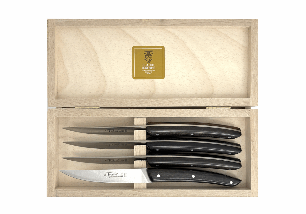 Un coffret en bois orné d’une étiquette dorée contient le « Coffret de 4 couteaux Le Thiers® Classique – Manche en bois d’ébène », composé de quatre couteaux à steak au manche en ébène, soigneusement rangés dans des emplacements individuels.